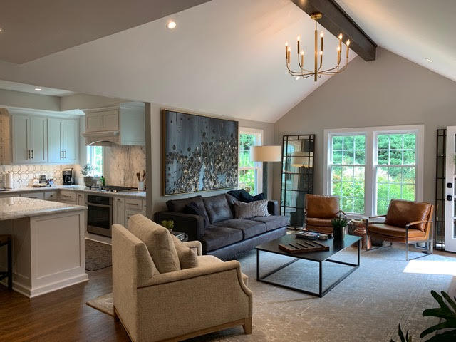 An open living space with vaulted ceilings, a modern chandelier, and a cozy seating area near large windows and a stone fireplace | Dusty Rhodes.