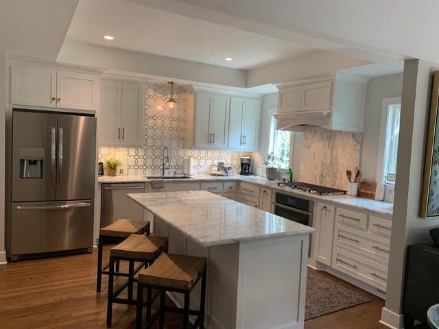 A contemporary kitchen with white cabinetry, a marble backsplash, stainless steel appliances, and a spacious island with seating | Dusty Rhodes.